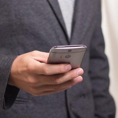 英語のビジネスメール、書き出しについての記事中のイメージ画像です。ジャケット姿の男性が片手でスマートフォンを操作しています。