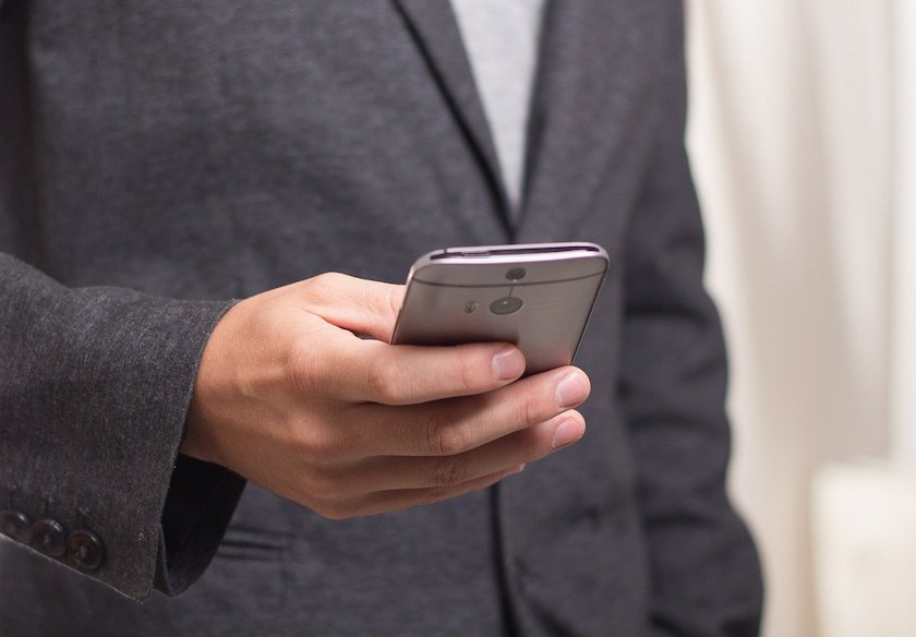 英語のビジネスメール、書き出しについての記事中のイメージ画像です。ジャケット姿の男性が片手でスマートフォンを操作しています。